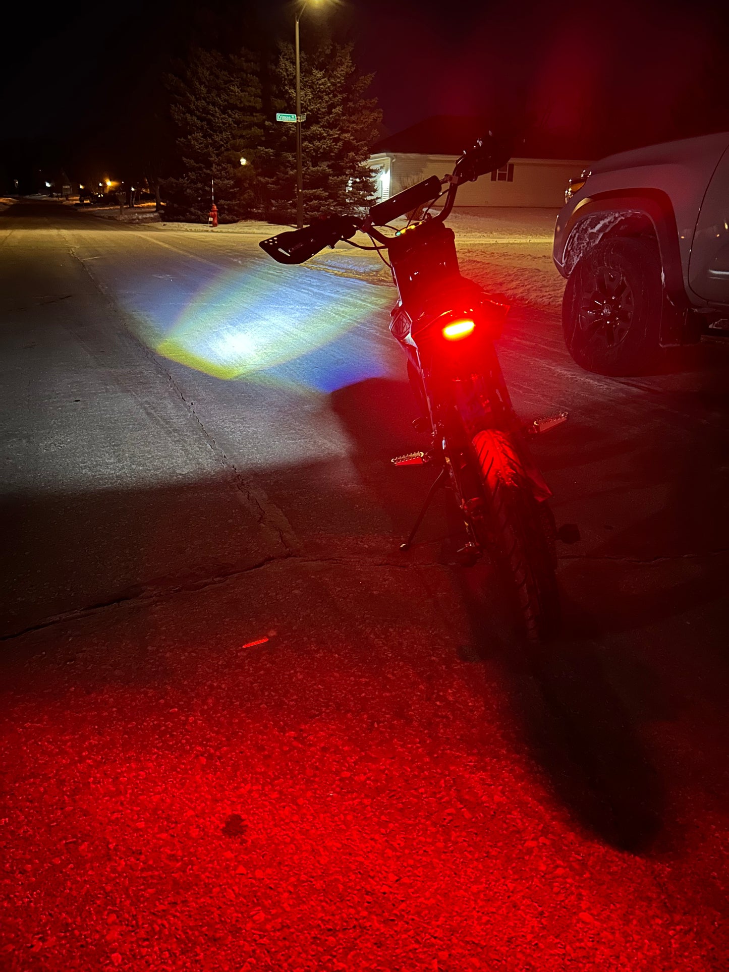 Surron Hyper Bee with headlight and taillight illuminated dark street at night.